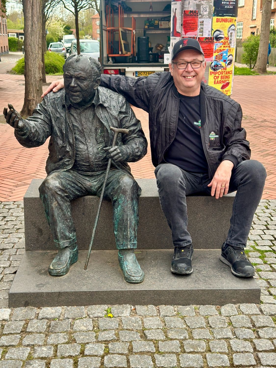 En fra Bodegakongen på bænken ved siden af en bronzestatue