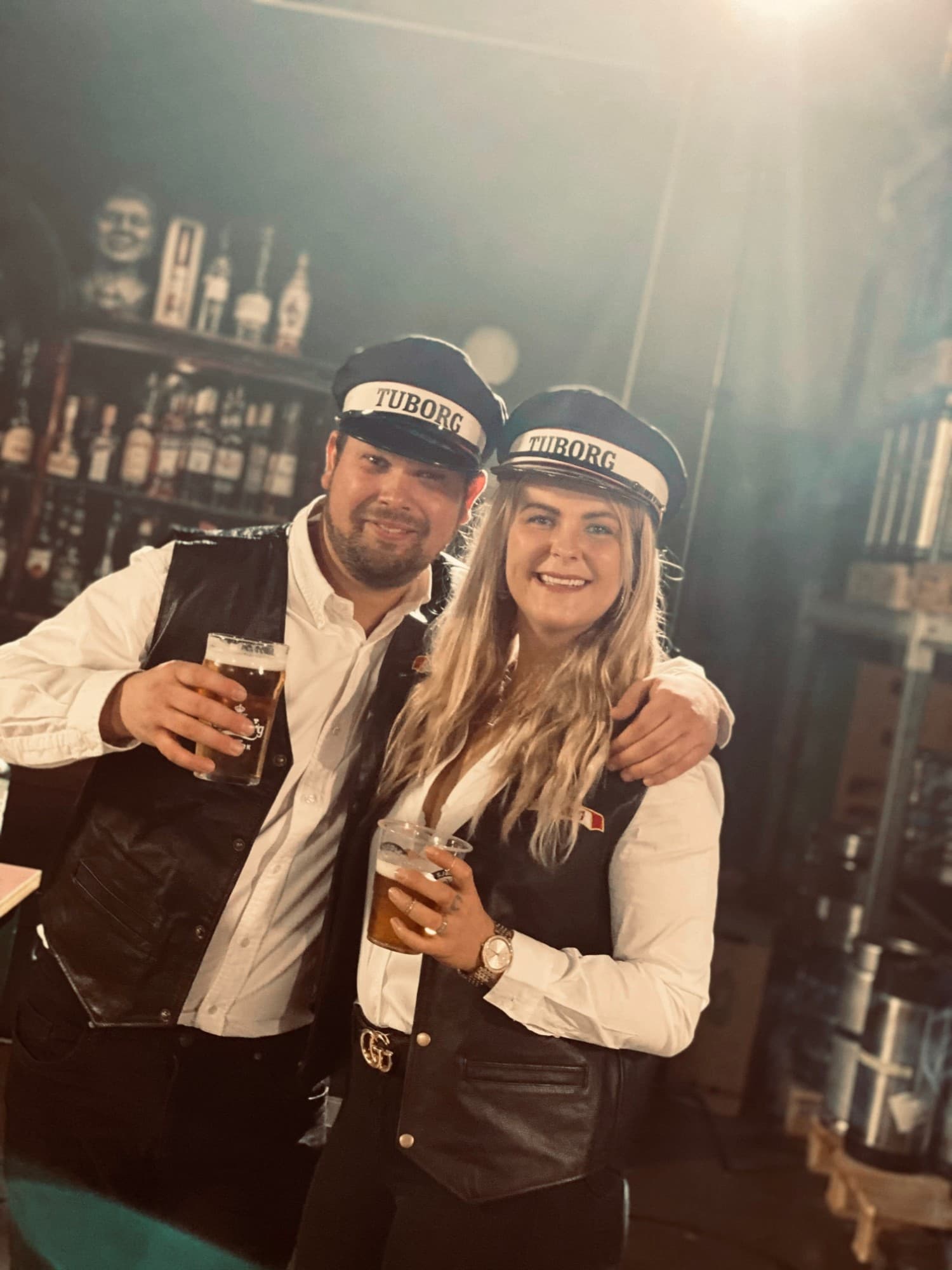 To af Bodegakongens tjenere i læderveste og Tuborg-kasketter skåler med fadøl